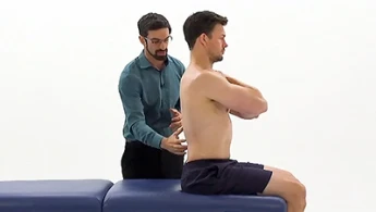 Physical therapist assessing seated patient for mobility and relative stiffness imbalance during physical exam.